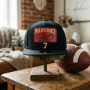 Example of a completed custom football hat: black flat bill snapback with a red leather patch, football helmet design, and gold-embroidered name MARTINEZ and number 7